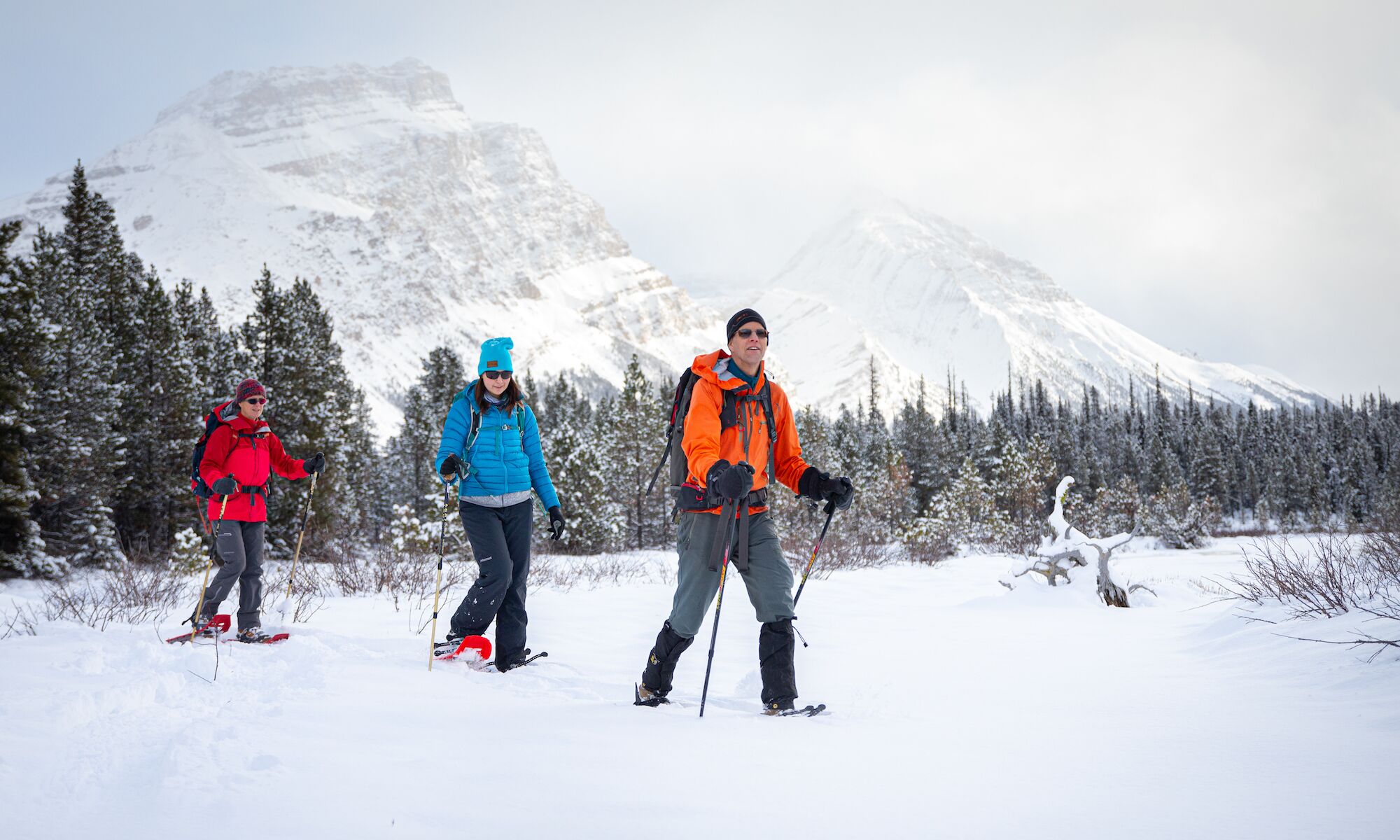 Three peopel going on a snowshoeing adventure in Banff National Park with mountains in the background.